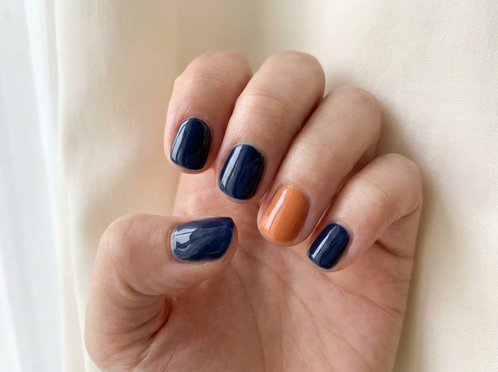 A muted orange ring nail contrasts with four glossy navy nails.