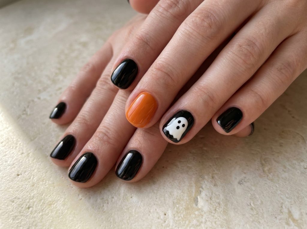 Short black Halloween nails with an orange accent and a white ghost on the ring nail.