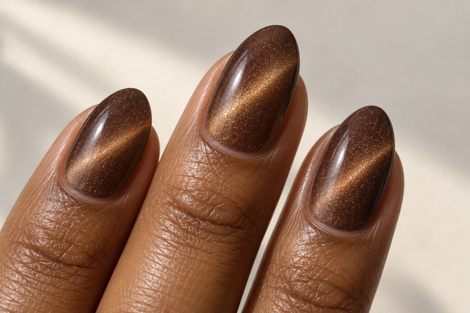 Mocha almond nails with bronze diagonal cat-eye reflections.