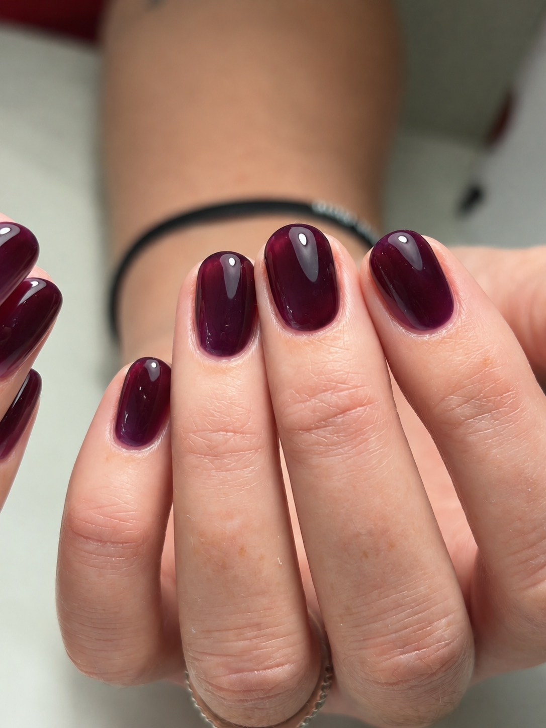 Short rounded nails with glossy sheer blackberry-purple polish.