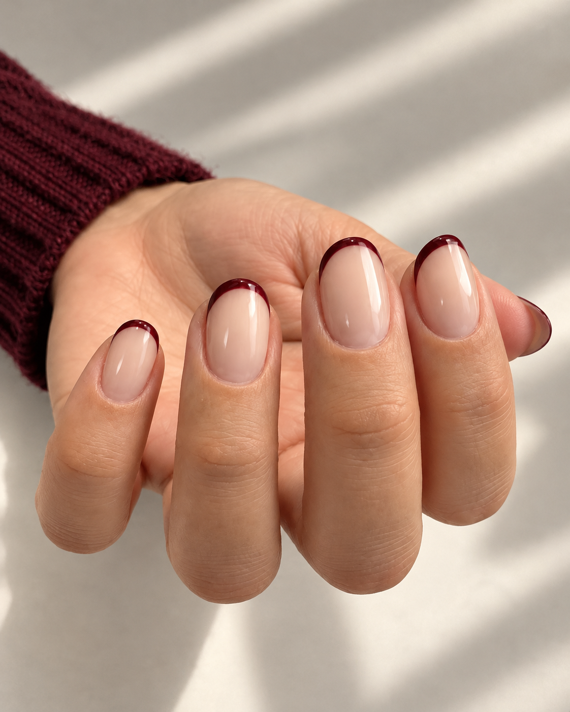 Short rounded beige nails with thin burgundy French tips.