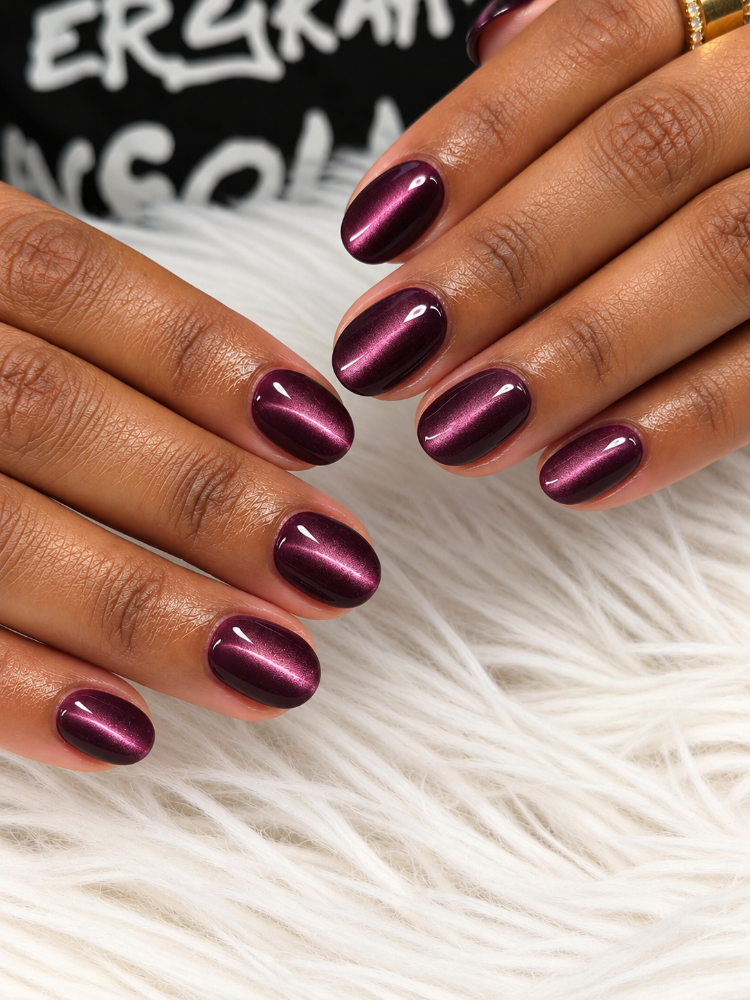 Short plum nails with a fine diagonal lilac-pink cat-eye reflection.