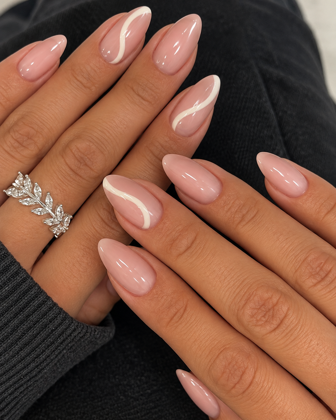 Nude almond nails with cream ribbon curves on the index and ring fingers.
