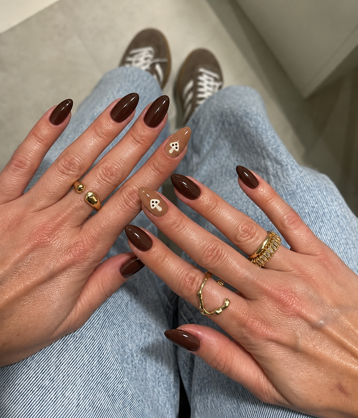 Deep brown nails with a small cream mushroom on a caramel ring-finger accent.