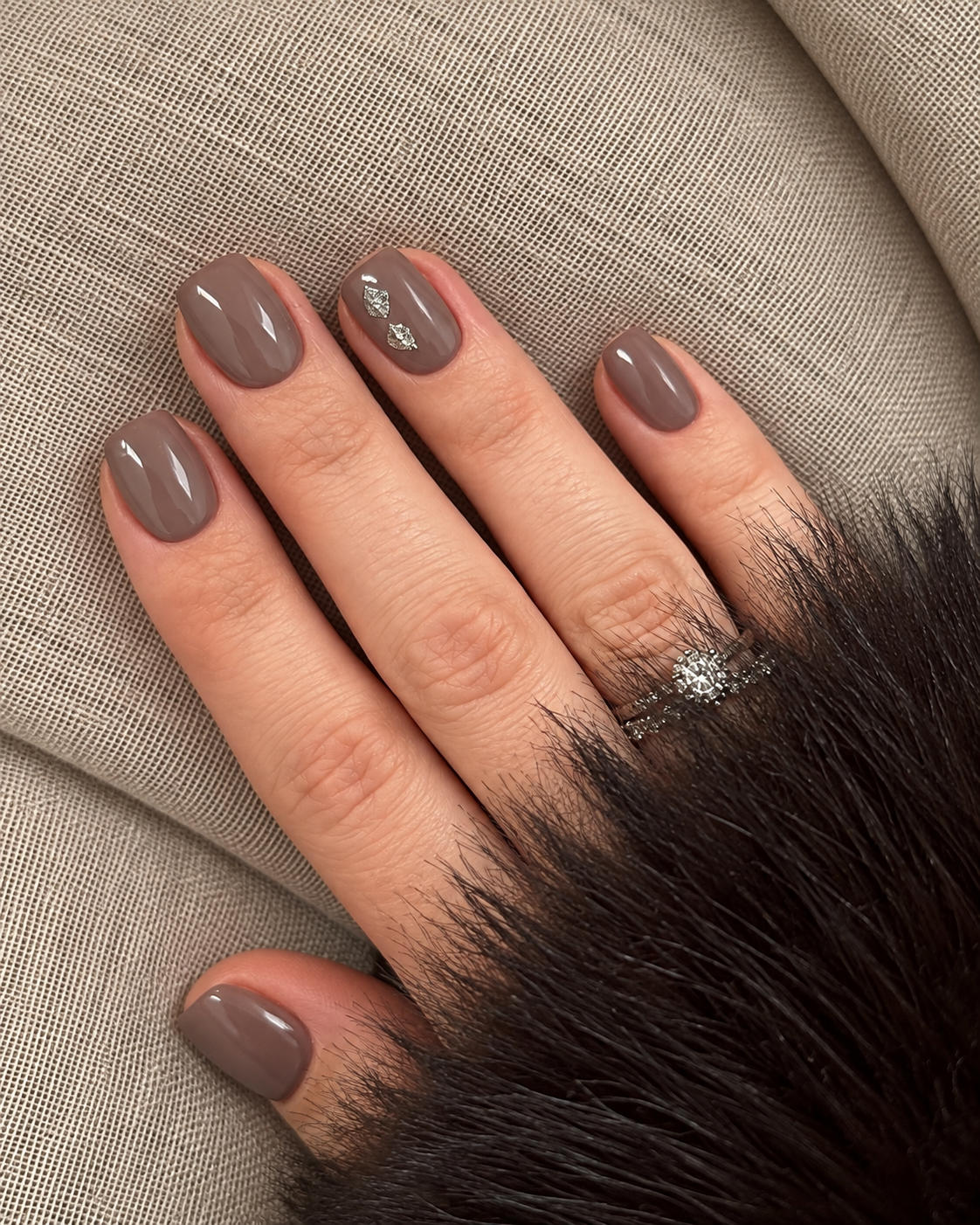Taupe nails with two small pewter foil flecks on the ring finger.