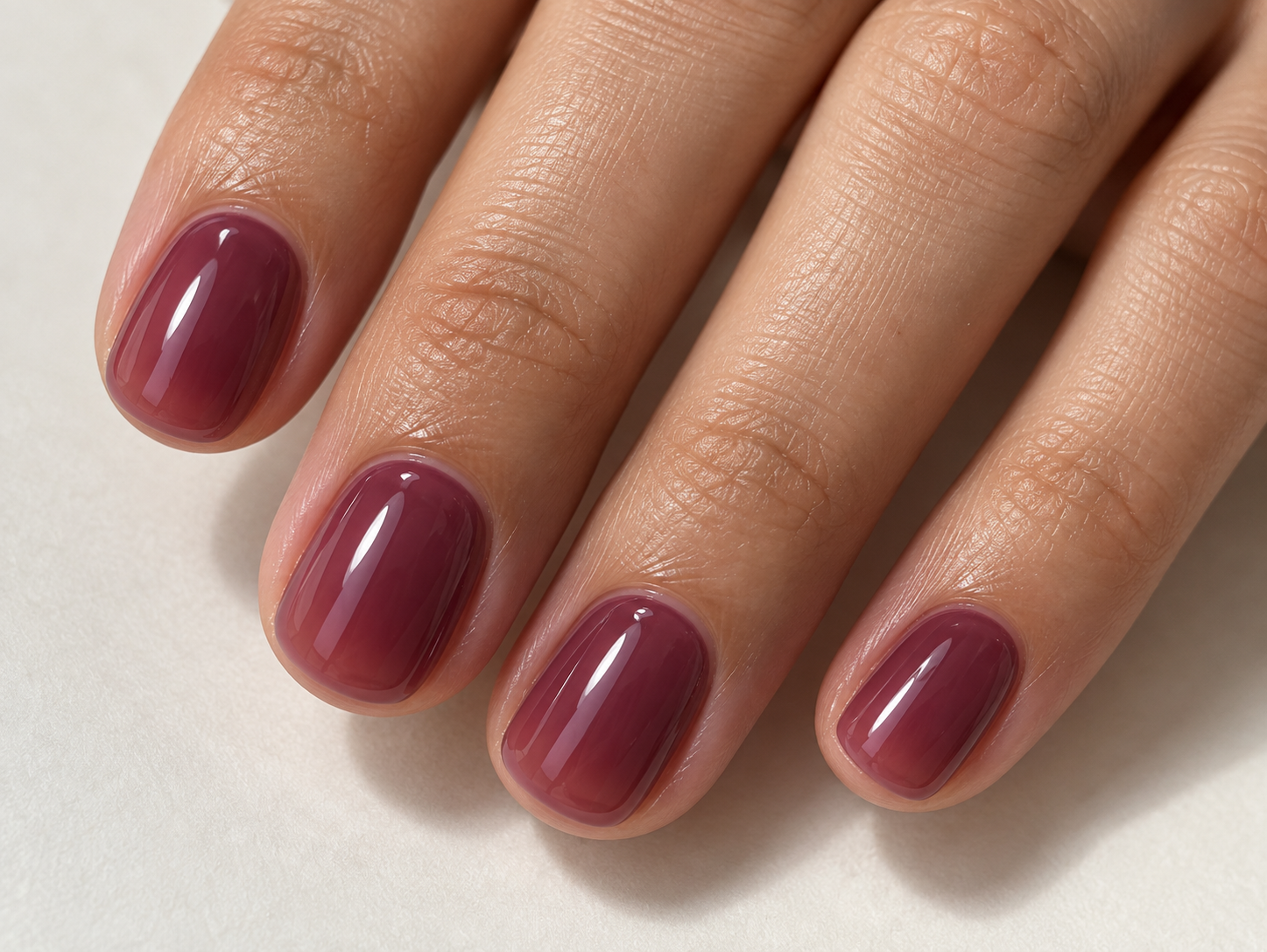 Short rounded nails with translucent mulberry-purple polish and a glossy jelly finish.