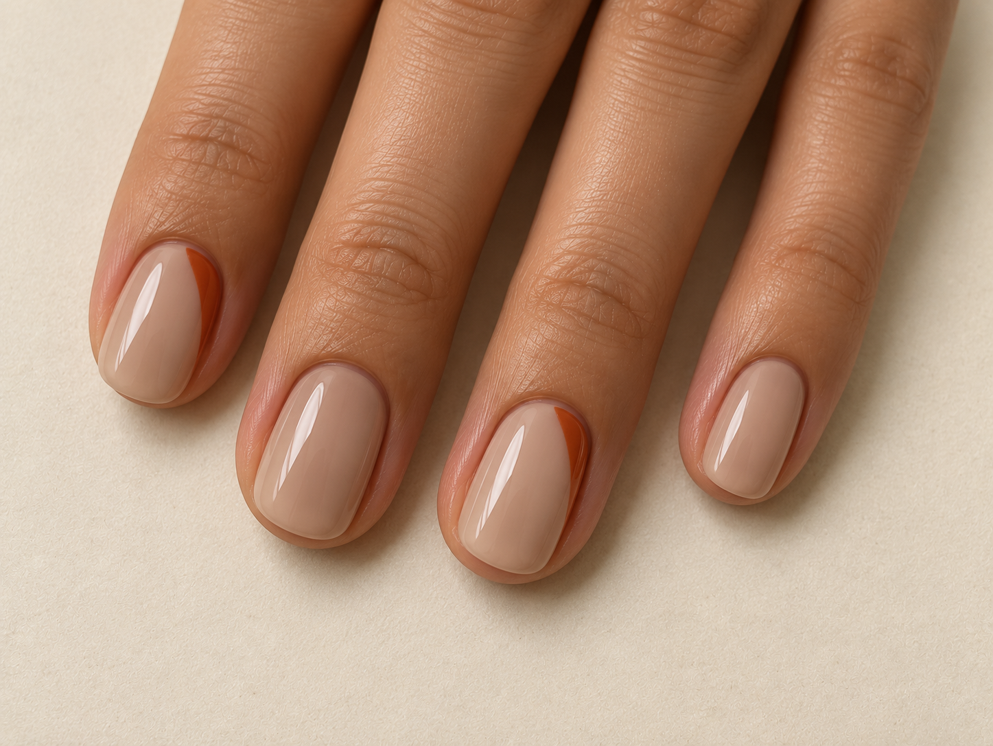 Short sheer-beige nails with narrow rust-colored side tips on the index and ring fingers.