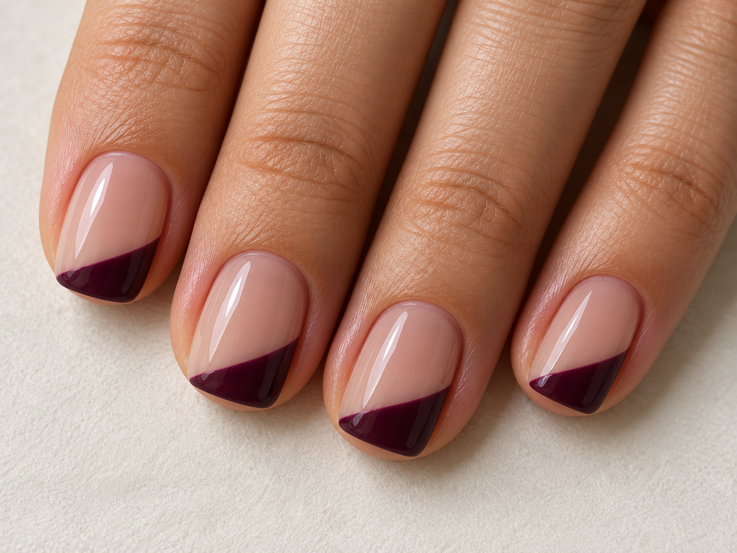 Short nude nails with shallow aubergine diagonal tips across the free edges.