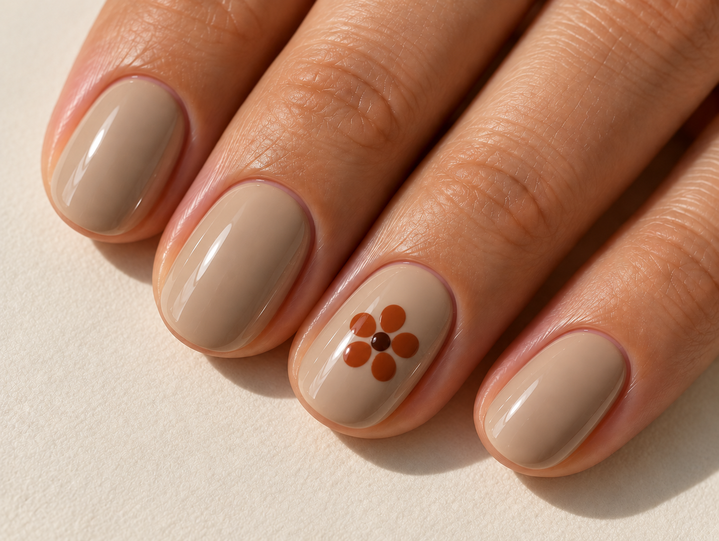 Short oat-beige nails with one five-petal terracotta flower and a dark brown center on the ring fingernail.