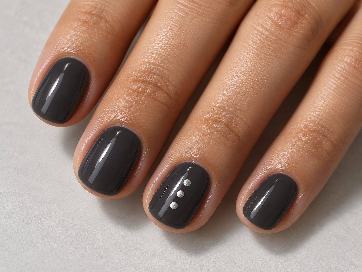 Short glossy charcoal nails with three small flat silver dots in a vertical line on one ring fingernail.