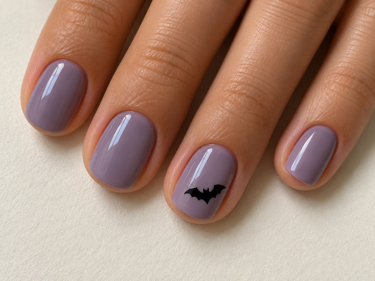 Short smoky-lilac nails with one small black bat silhouette on the ring fingernail.