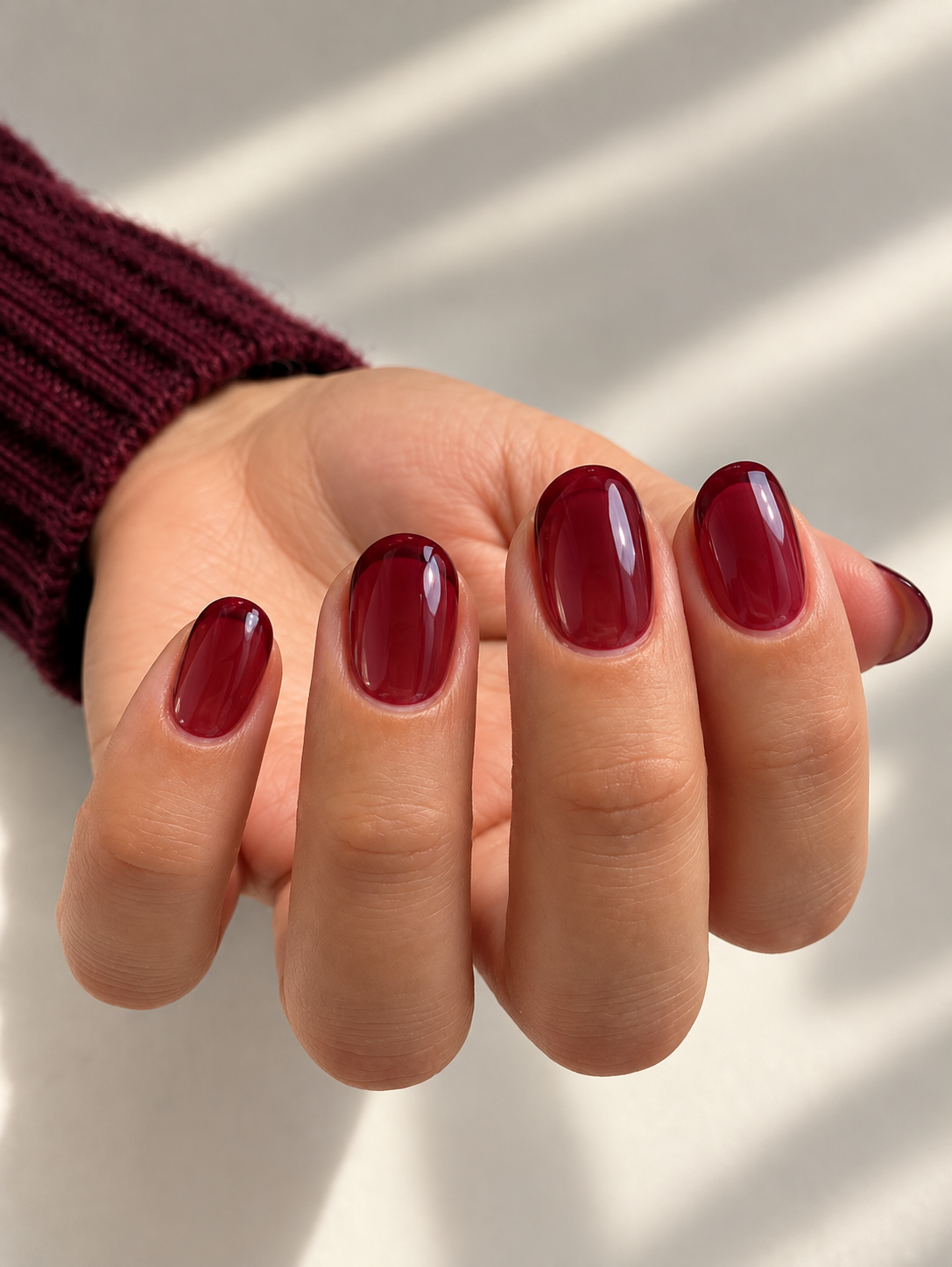 Short rounded nails with translucent cranberry jelly polish and a glossy finish.