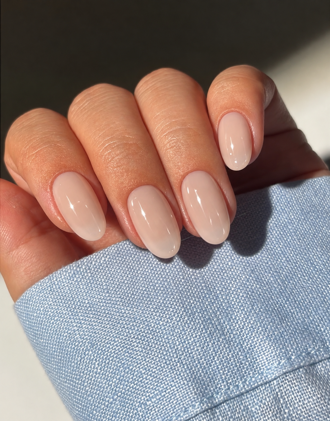 Short oval nails with sheer warm oat-beige polish and a soft glossy finish.