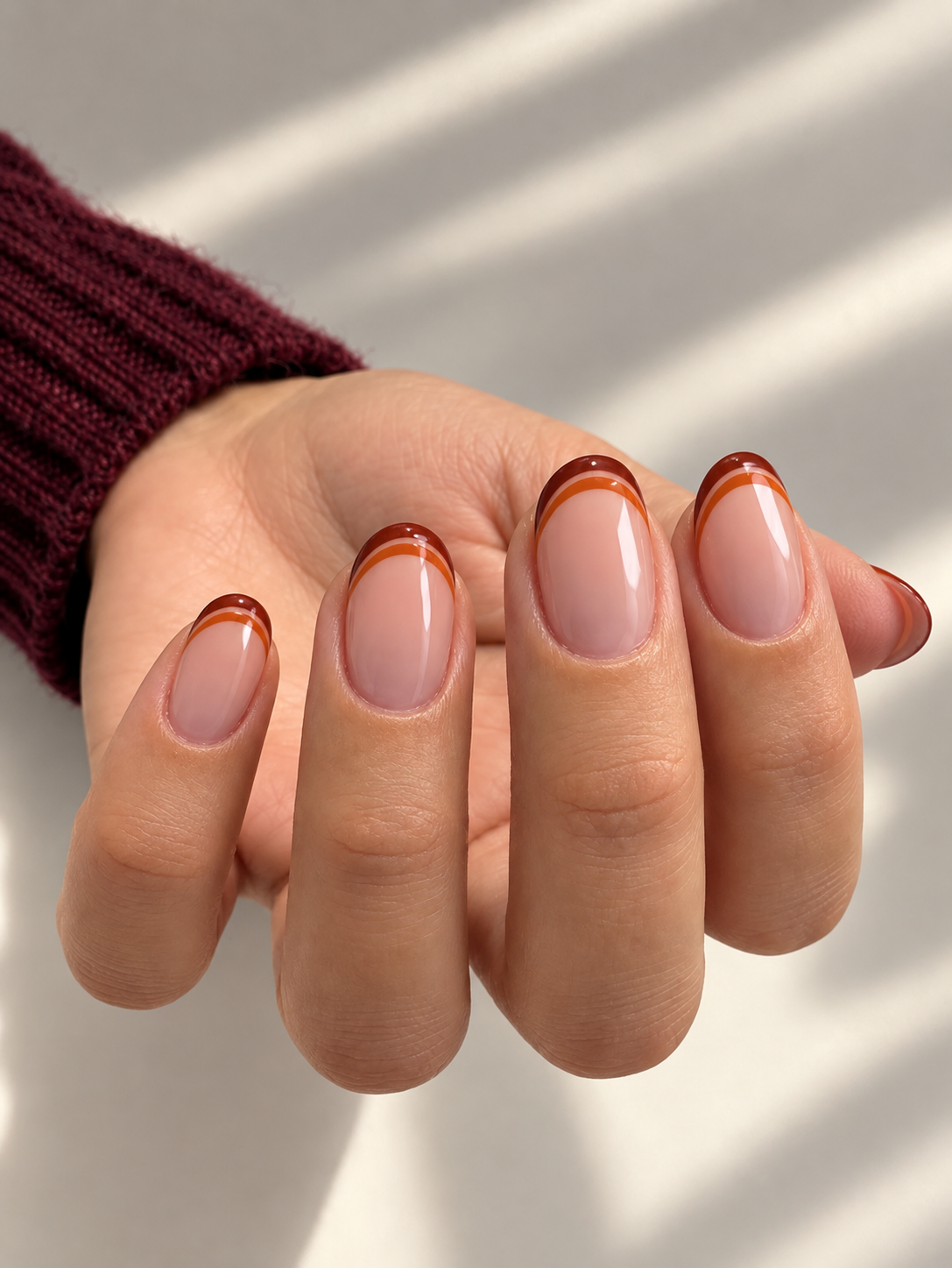 Oval nude nails with separate pumpkin-orange and rust lines tracing the tips.