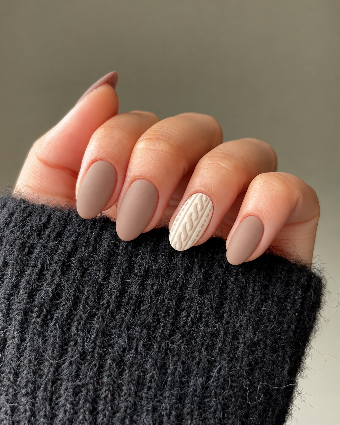 Matte mushroom-beige nails with a cream ring-finger nail bearing a flat beige cable-knit pattern.