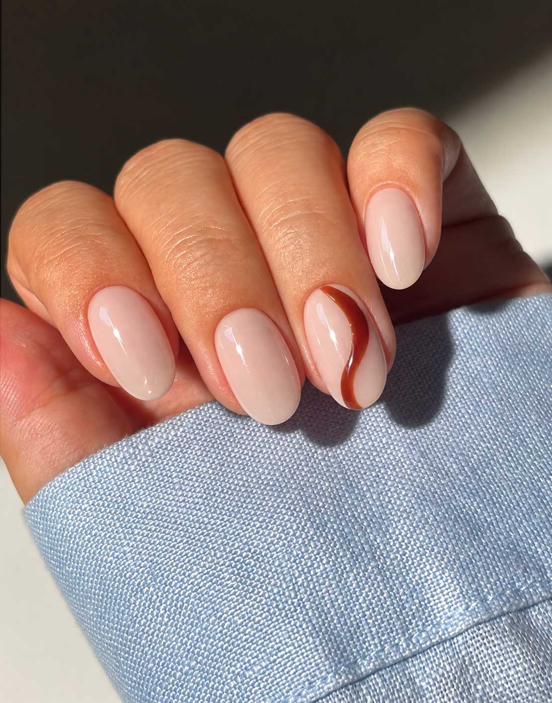 Milky beige oval nails with a single russet curve on the ring finger.