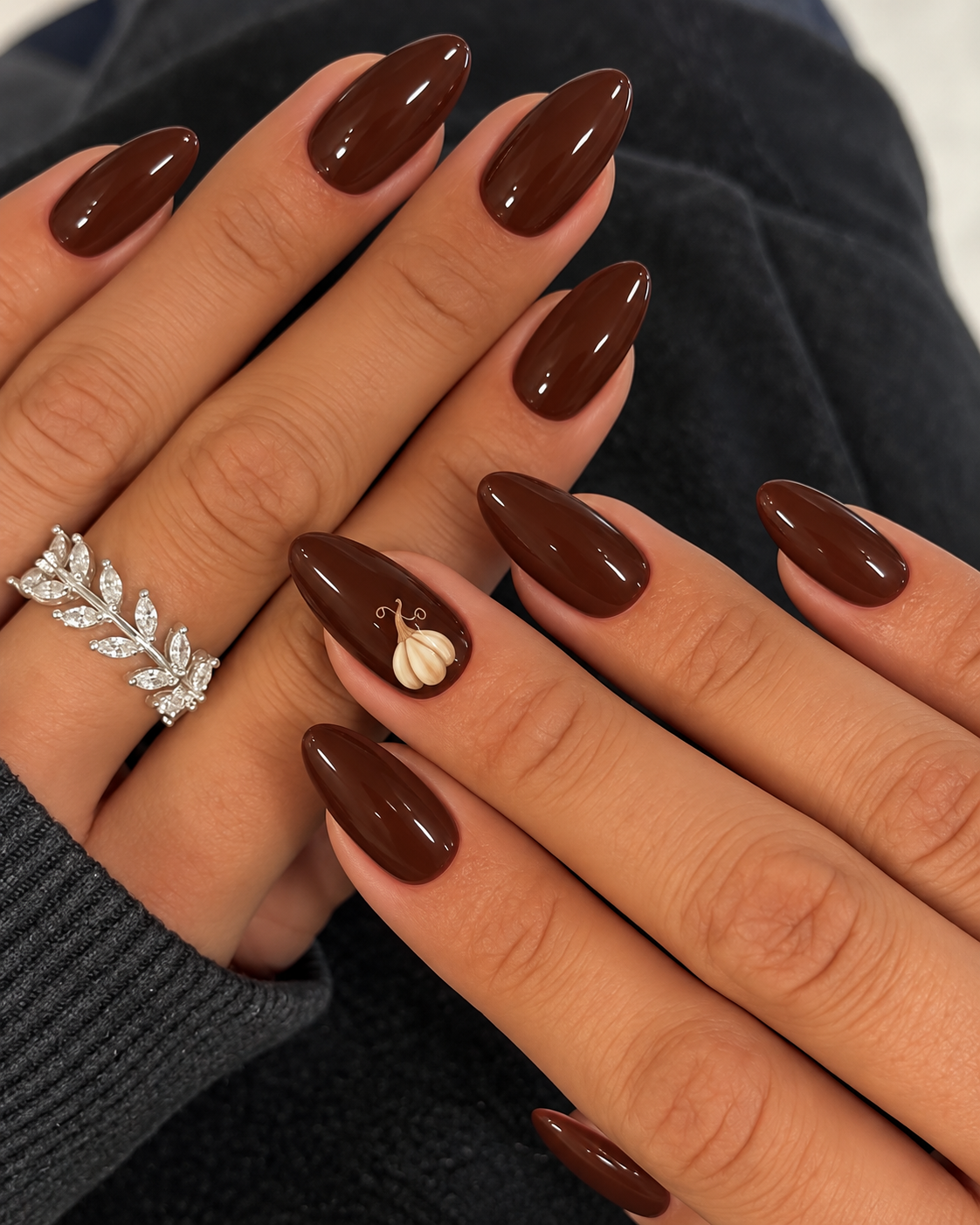 Glossy chocolate nails with a small cream gourd on the ring finger.
