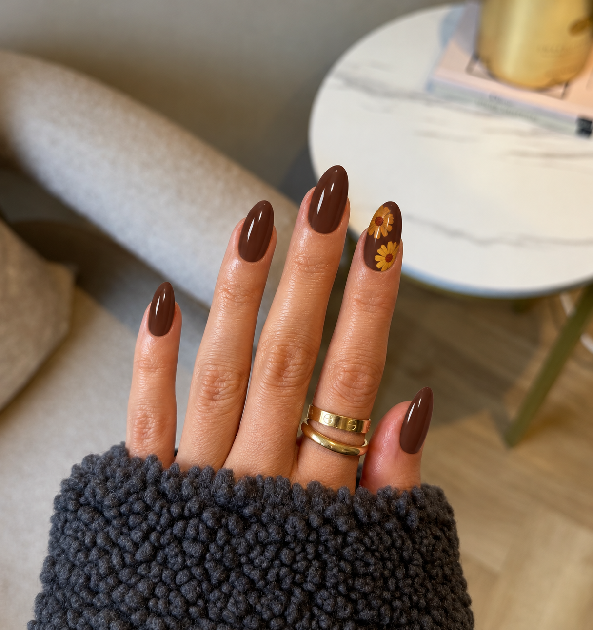 Cocoa oval nails with two muted marigold flowers and rust centers on the ring finger.