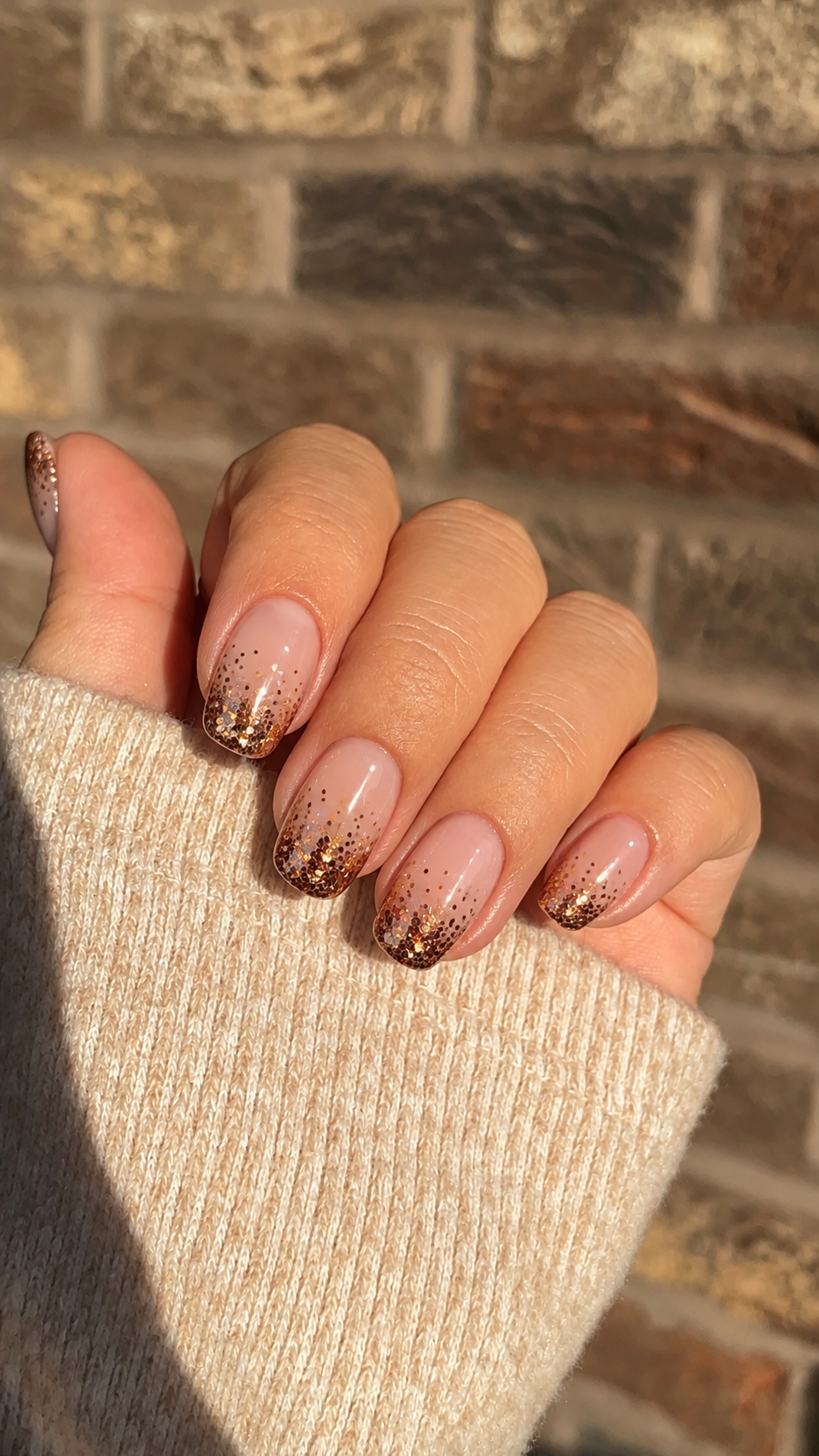 Short sheer nude nails with sparse bronze glitter fading down from the tips.